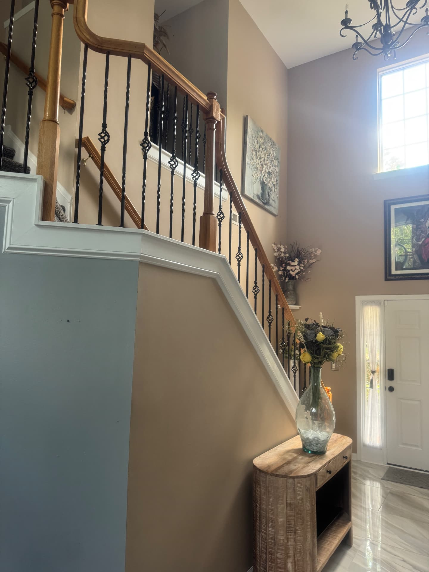 Two story foyer after with soft greige walls, wrought iron balusters and polished marble tile