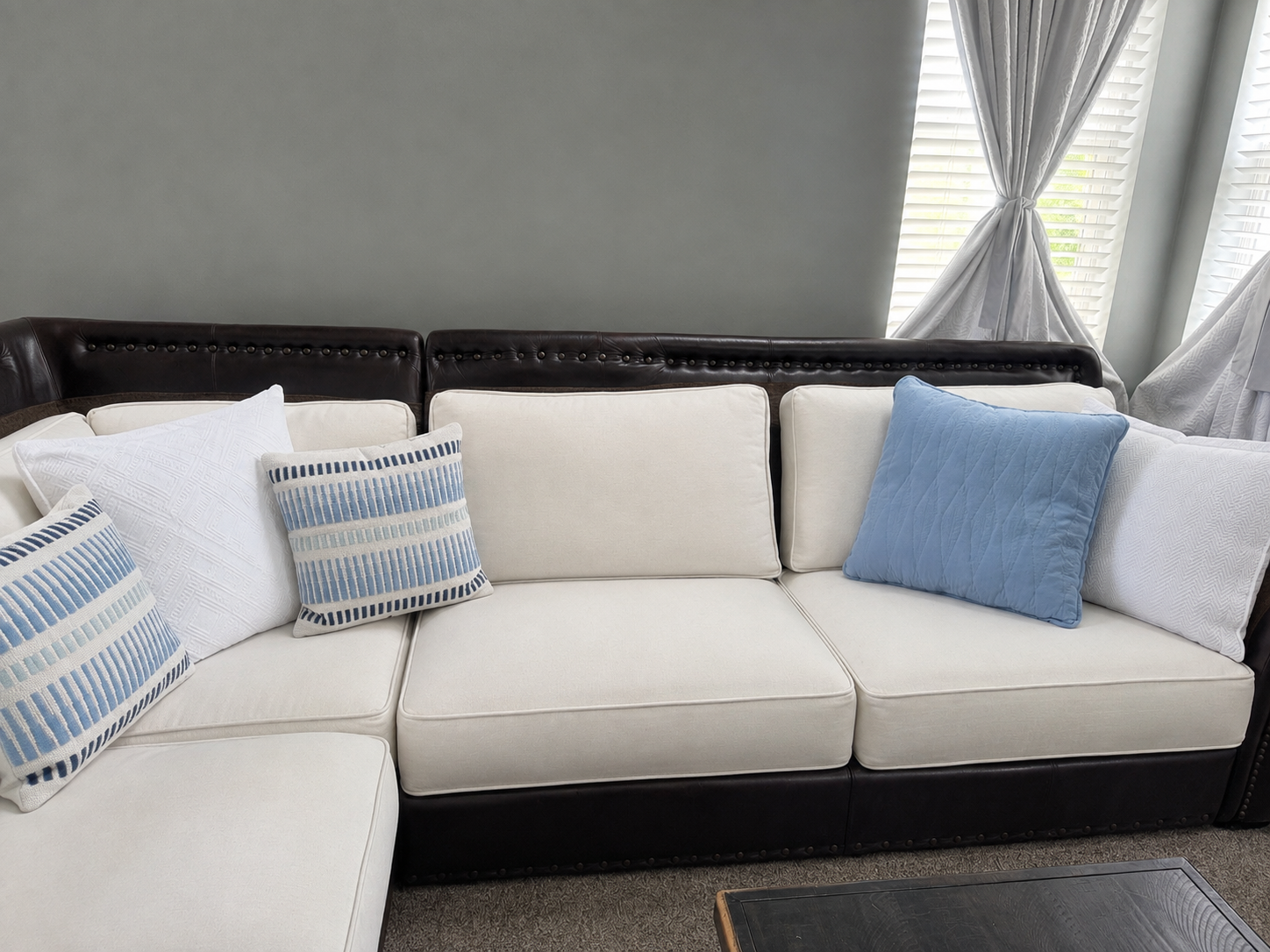 Sectional after with white linen cushions, blue and white textured pillows and pale grey drapery