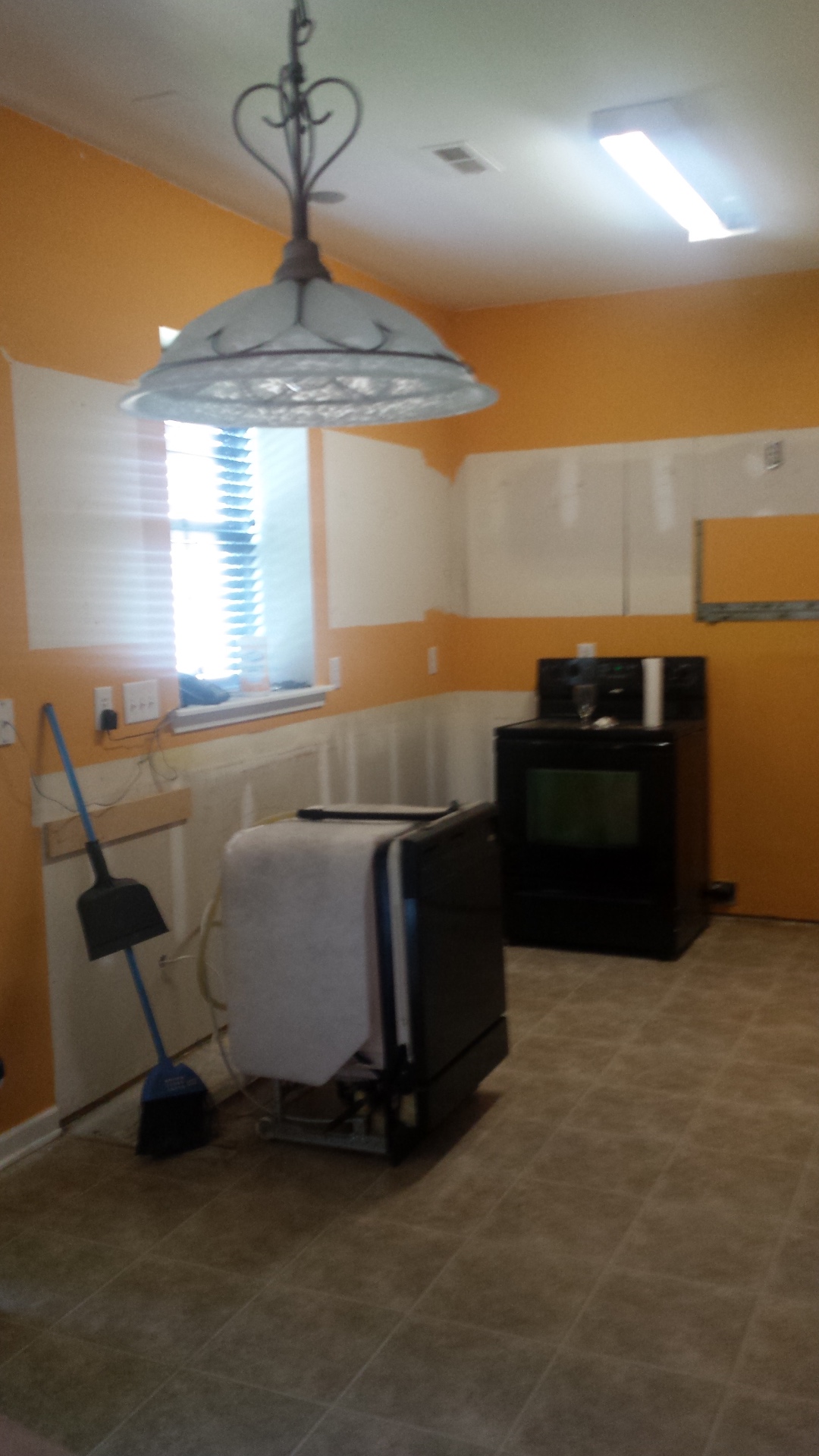 Kitchen before remodel with orange walls, bare drywall and dated vinyl flooring