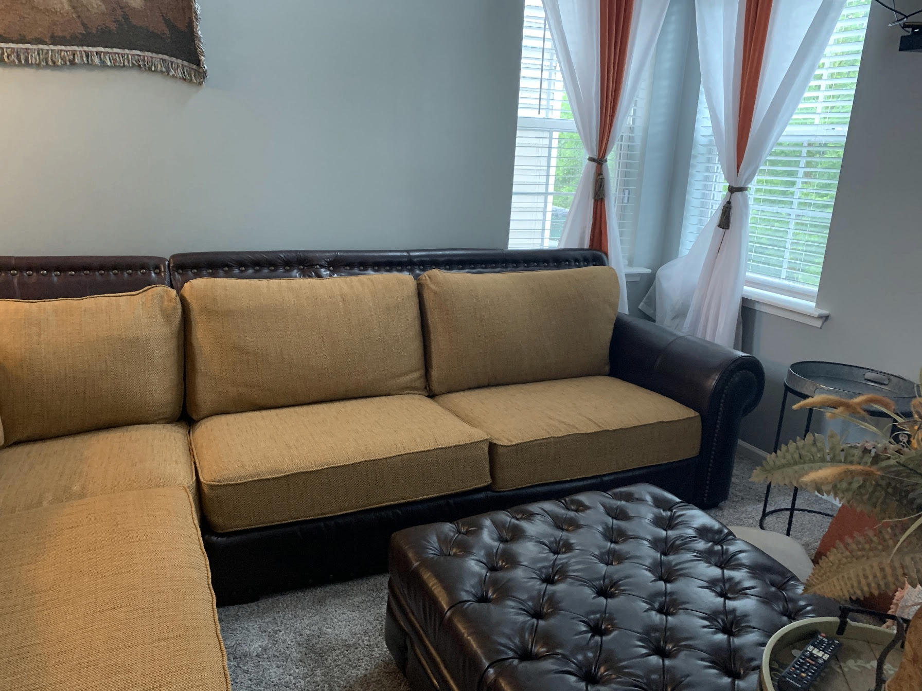 Living room before with gold tweed sectional, brown leather ottoman and orange curtains