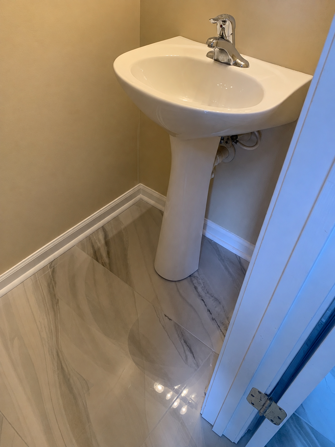 Powder room with pedestal sink over polished marbled tile flooring