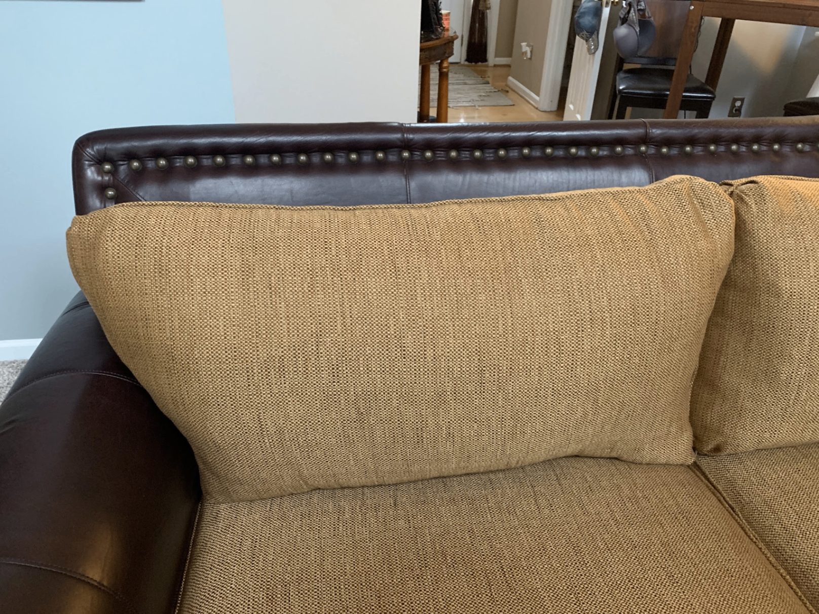 Close up of the sectional before with worn gold tweed cushions and brown leather nailhead frame